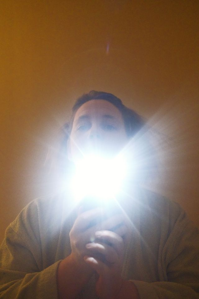 a photograph of a man holding a light up to his face