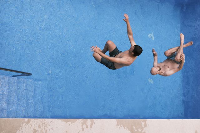 a photograph of two men are swimming in a pool with their hands up